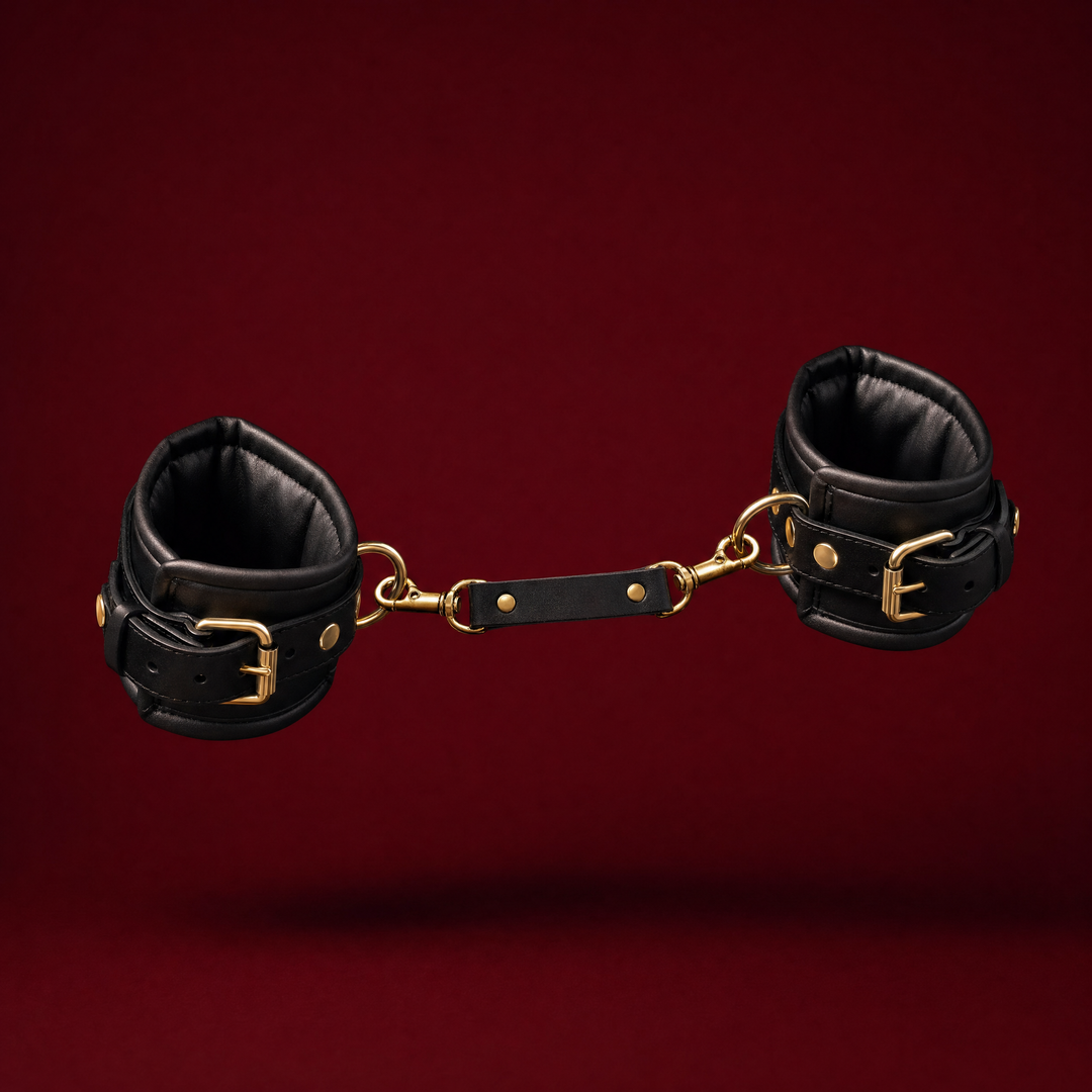 Bijou padded restraint cuff pair in black with gold buckles and a clip-on connector strap