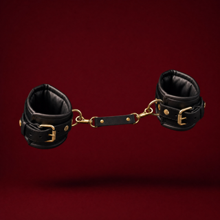 Bijou padded restraint cuff pair in black with gold buckles and a clip-on connector strap