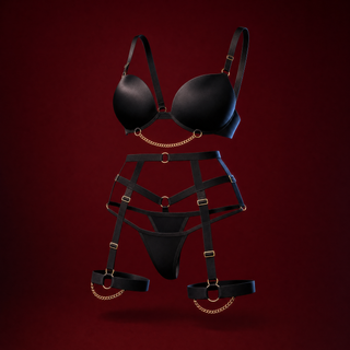 Rafaela black strappy lingerie set with gold rings and a draped gold chain, bra, garter belt, thong and thigh bands, on a deep burgundy background