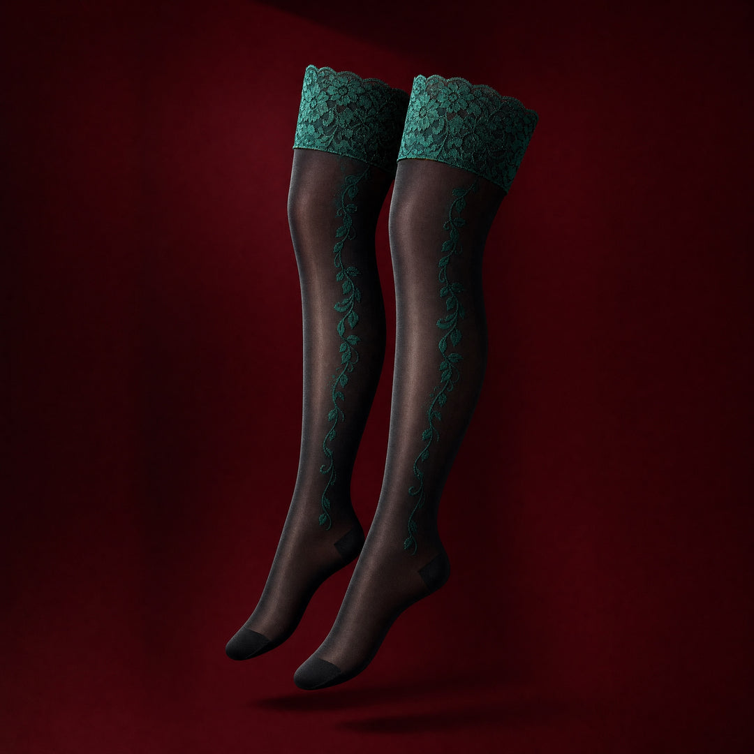 Soraya sheer black hold up stockings with wide emerald green lace tops and embroidered vine motif, on a deep burgundy studio background